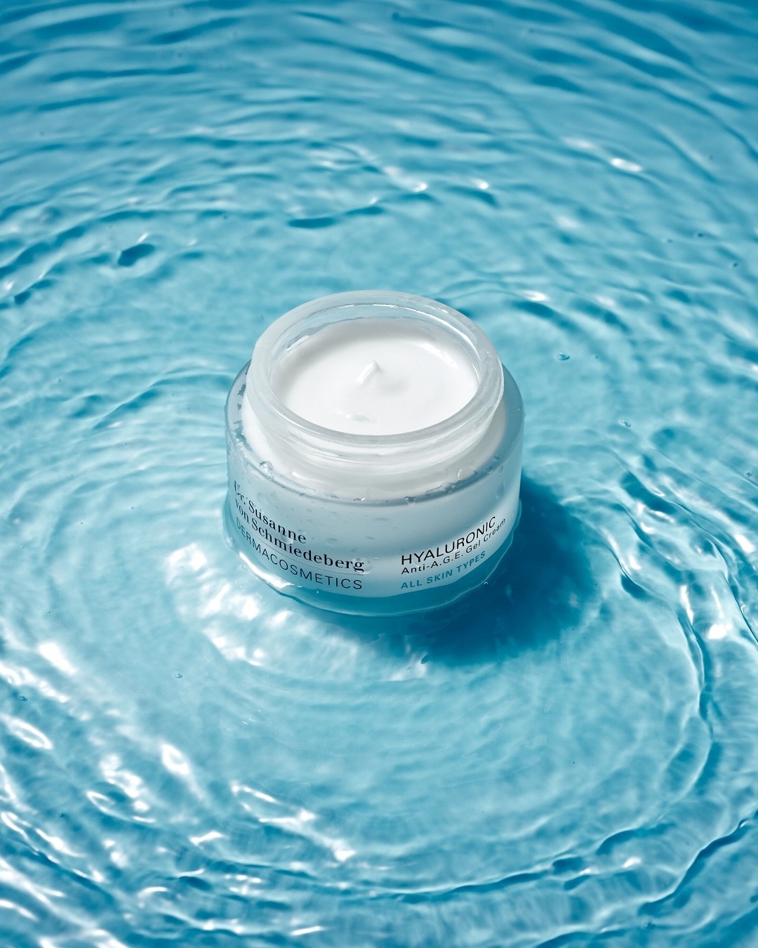 Eine durchsichtige Dose Dr. Susanne von Schmiedeberg Dermacosmetics Hyaluronic Anti-A.G.E. Gel Creme für alle Hauttypen schwimmt auf blauem Wasser.