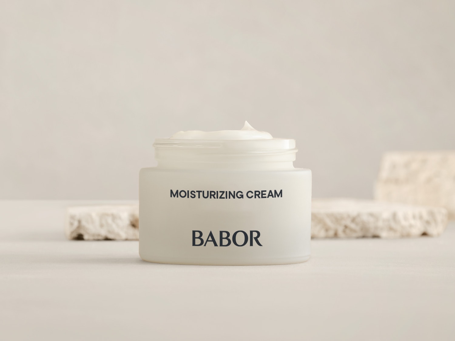 Krem nawilżający Babor w szklanym słoiczku z białą zawartością, obok niego znajdują się dekoracyjne kamienie.