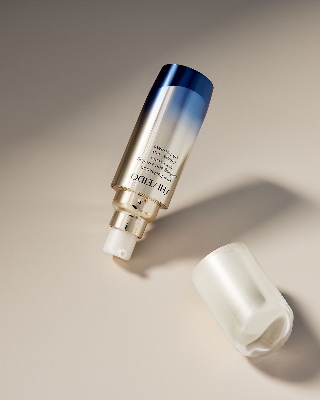 Krem pod oczy Shiseido Vital Perfection w złotym opakowaniu z gradientem od błękitu do granatu, obok leży transparentna nakrętka.