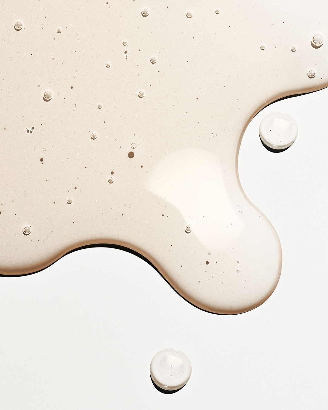 Nahaufnahme einer beigen, transparenten Flüssigkeit mit kleinen Bläschen, die eine glatte, leicht klebrige Textur suggeriert.