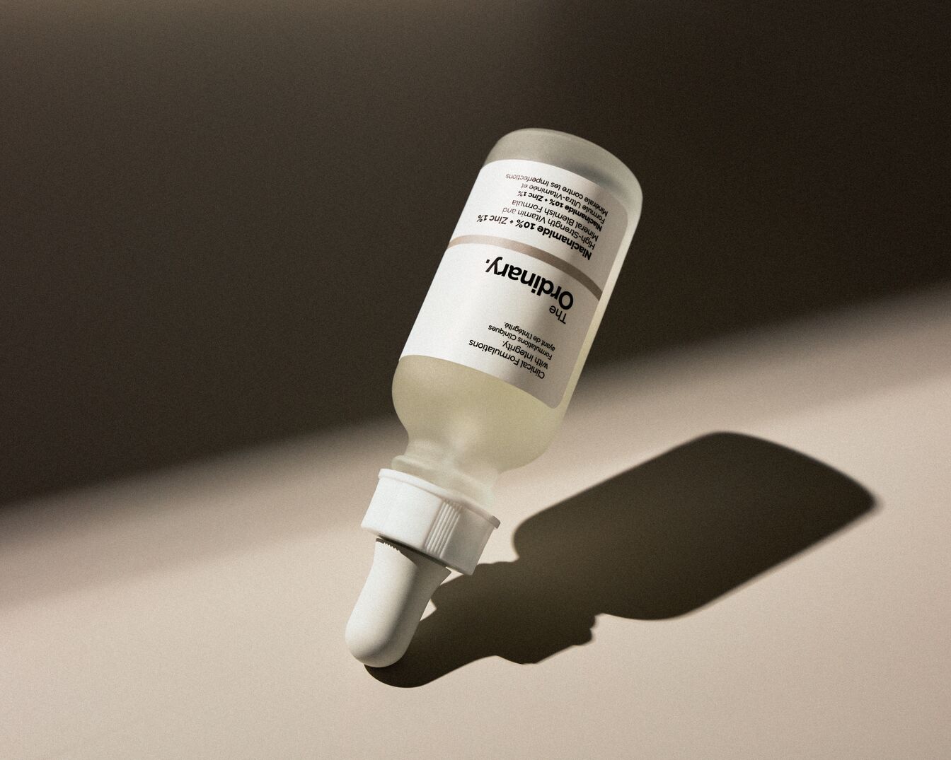 Das Ordinary Niacinamid 10% + Zink 1% Serum in einer durchsichtigen Glasflasche mit weißer Pipette liegt auf einer hellen Oberfläche und verspricht eine hochwirksame Vitamin- und Mineralstoffformel gegen Hautunreinheiten.