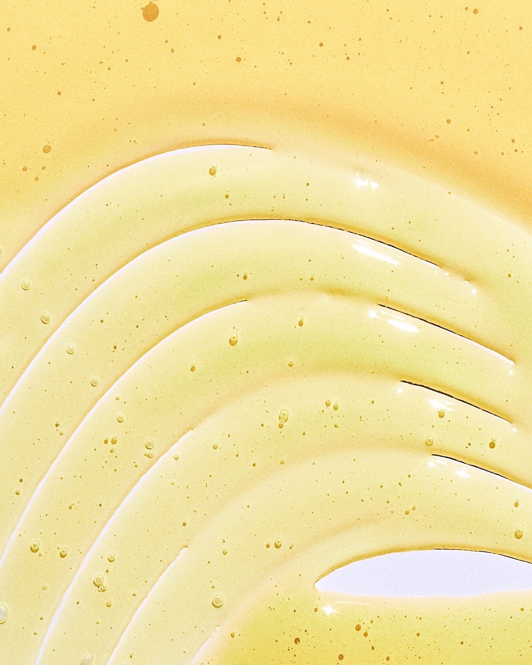 Gouden serum textuur met kleine luchtbelletjes, ideaal voor een stralende en gehydrateerde huid.