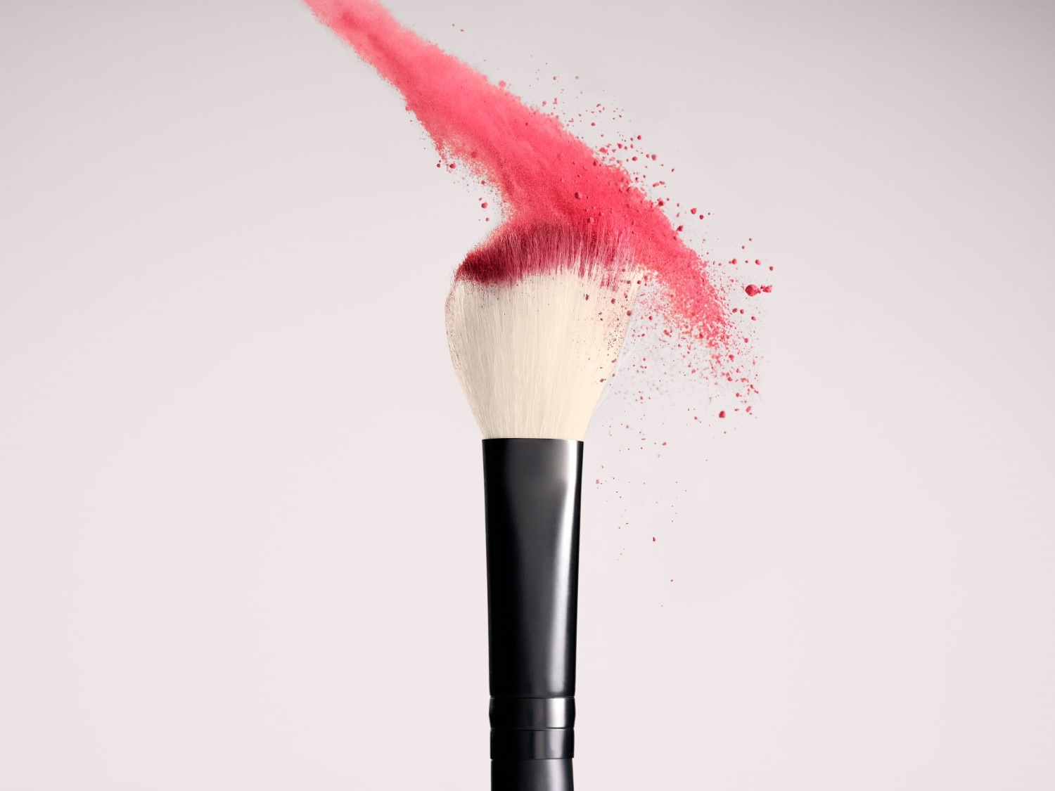 Ein Make-up-Pinsel mit schwarzem Griff und weißen Borsten ist mit rosa Puder bedeckt, der in der Luft zu schweben scheint.