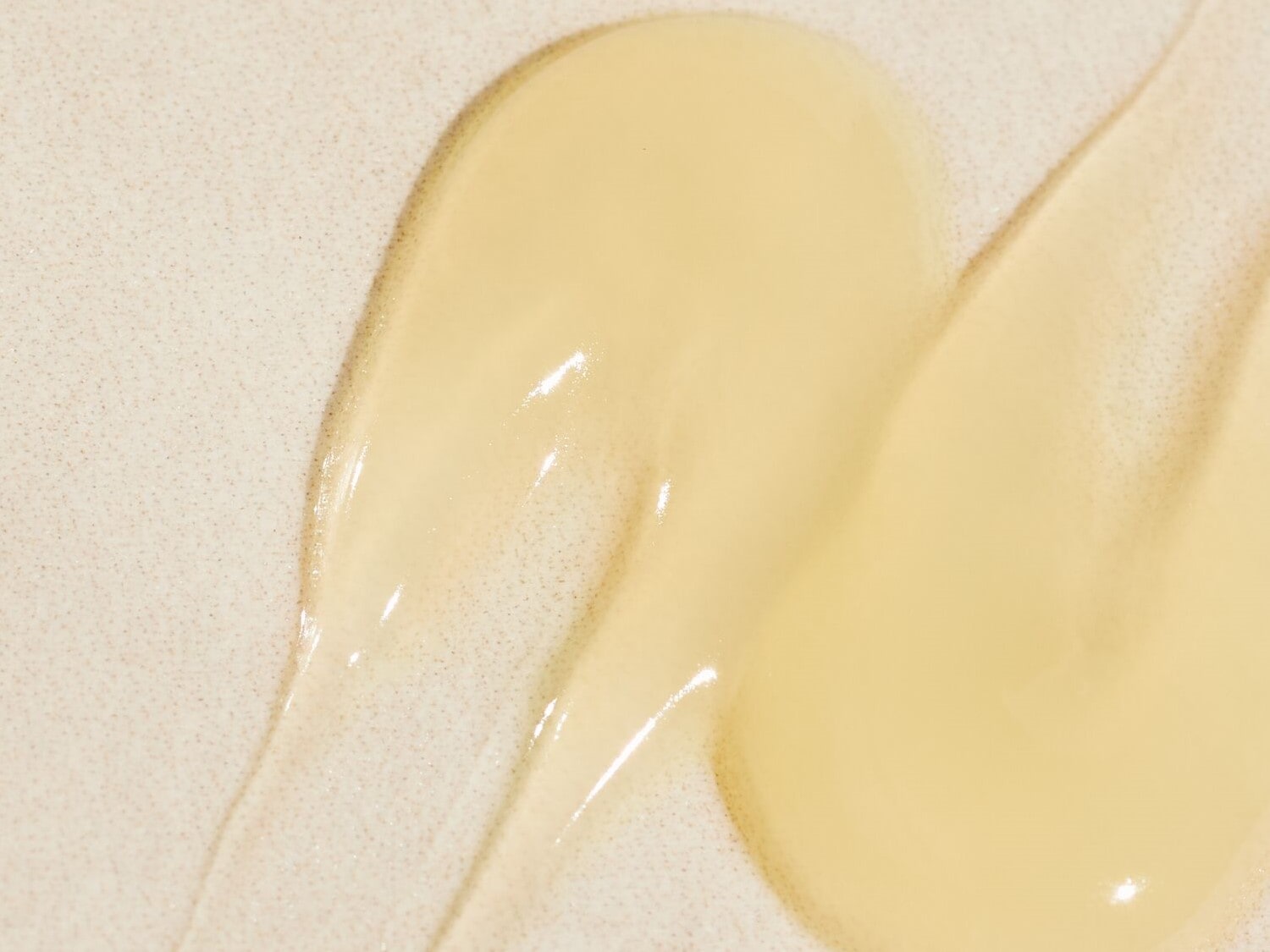 Nahaufnahme von zwei transparenten, hellgelben Gelklecksen auf einem beigen Untergrund, die eine glatte, leicht fließende Textur zeigen.