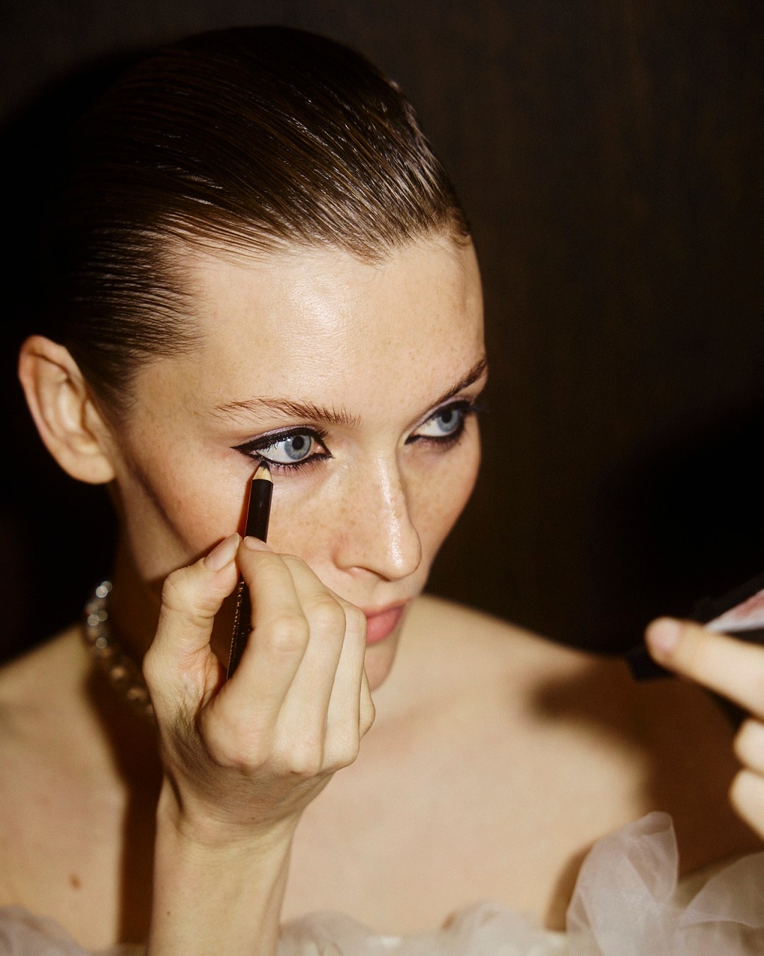 Šviesiaplaukė moteris su mėlynomis akimis tepa juodą akių kontūrą, kad paryškintų savo žvilgsnį.