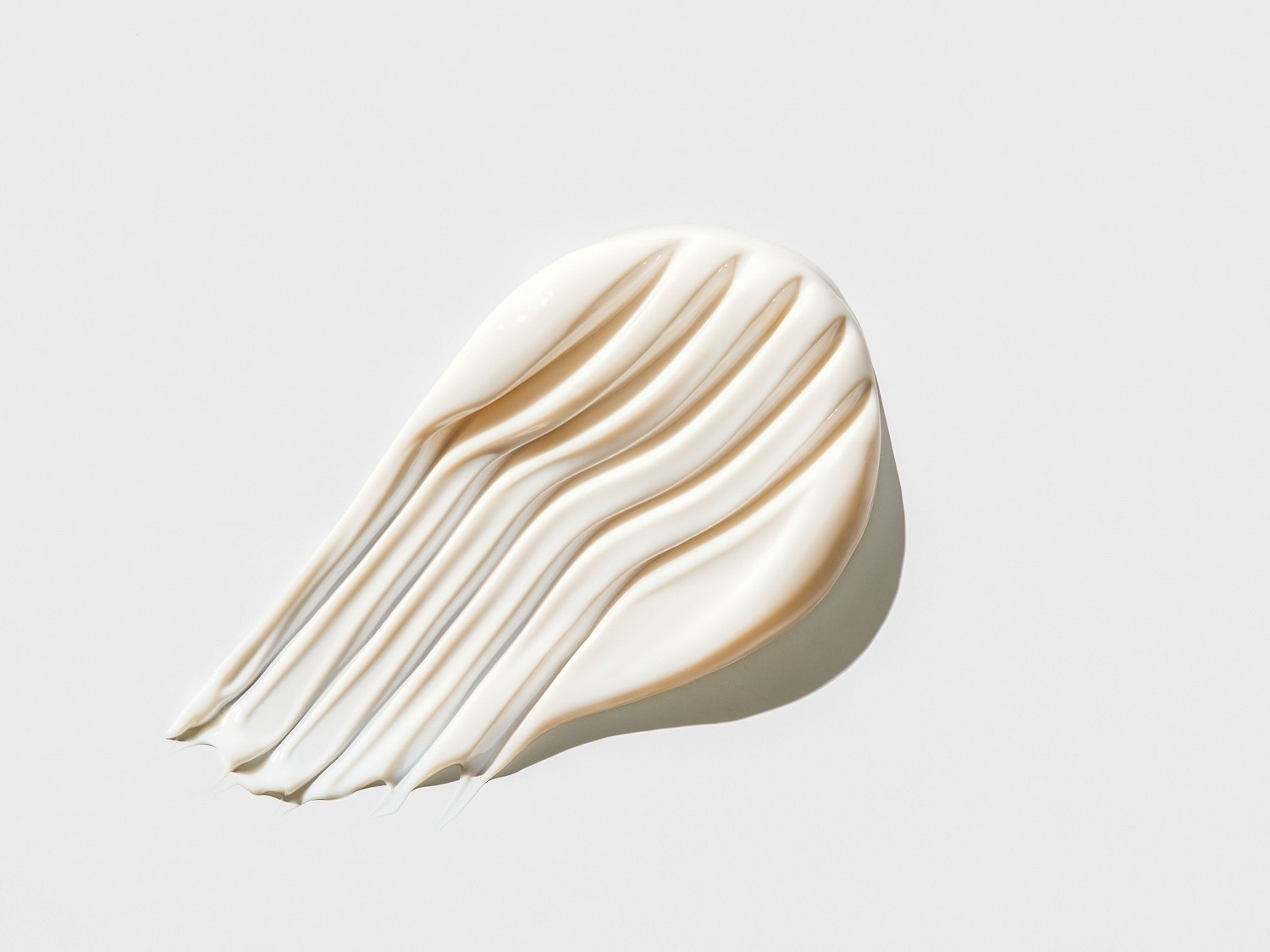 Texture crémeuse beige clair, étalée en larges vagues sur un fond blanc, évoquant douceur et hydratation pour la peau.