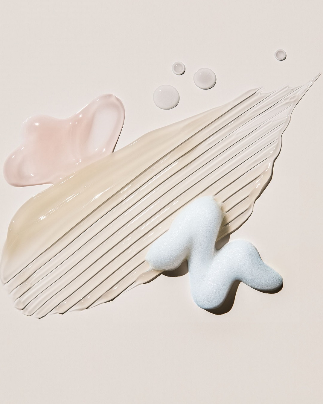 Verschiedene Texturen von Schönheitsprodukten, darunter ein rosa Gel, eine beigefarbene Creme mit Streifen, ein blauer Schaum und klare Tropfen, die die Vielfalt der verfügbaren Formeln zeigen.