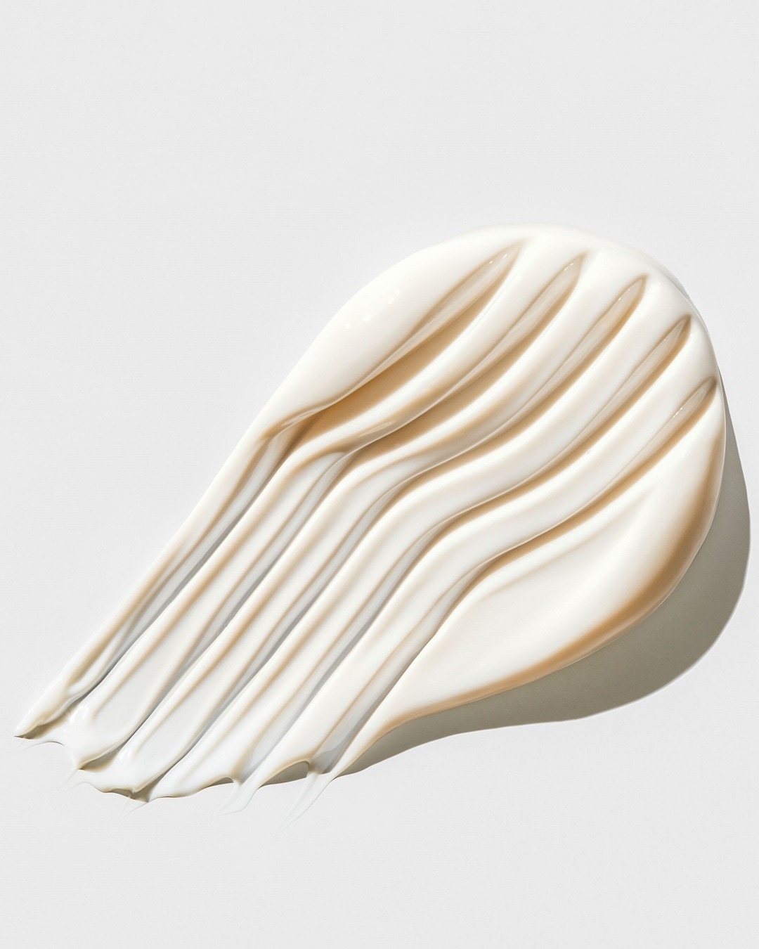 Nahaufnahme eines cremefarbenen Kosmetikprodukts mit glatter Textur, das in einer dicken Schicht aufgetragen wurde und dessen Oberfläche sanfte Wellen bildet.