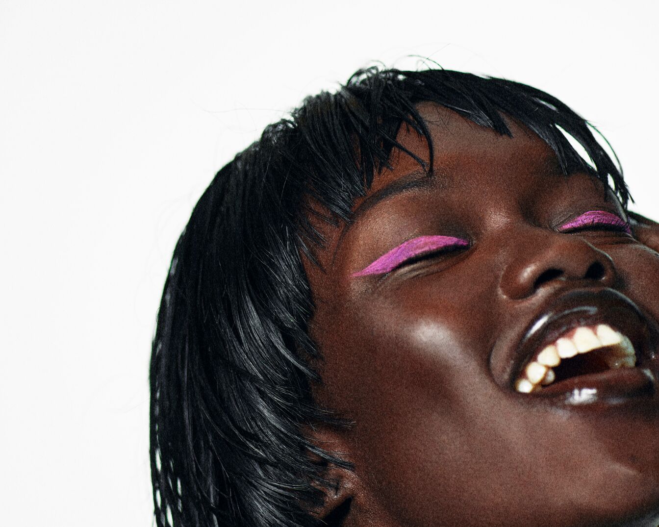 Nahaufnahme einer dunkelhäutigen Frau mit geschlossenen Augen und einem strahlenden Lächeln, akzentuiert durch einen auffälligen, pinkfarbenen Eyeliner.