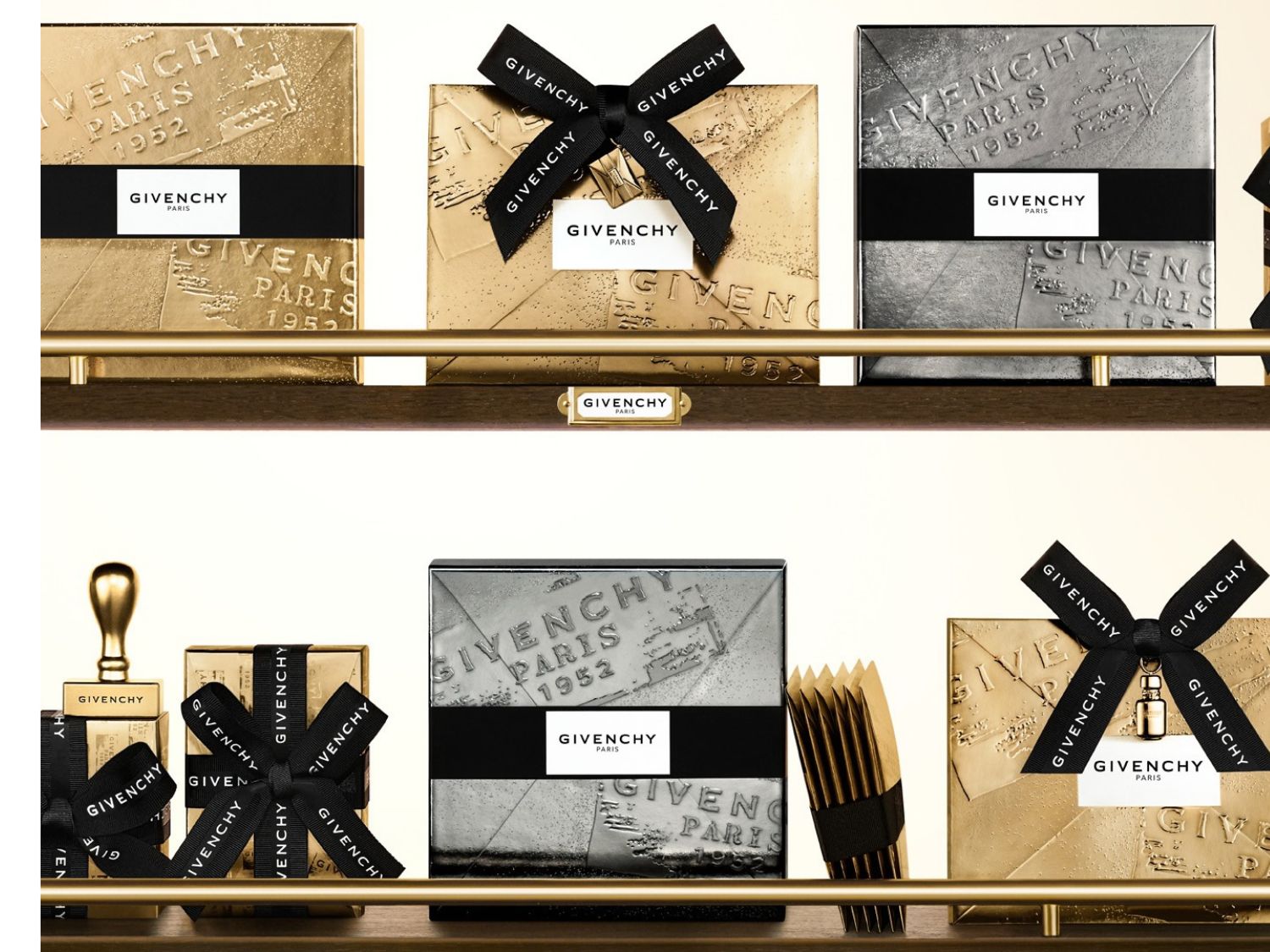 Drei goldene und silberne Givenchy-Geschenkboxen mit der Aufschrift "Givenchy Paris 1952" sind auf einem Regal ausgestellt, wobei die goldene Box mit einem schwarzen Band mit dem Givenchy-Logo verziert ist.