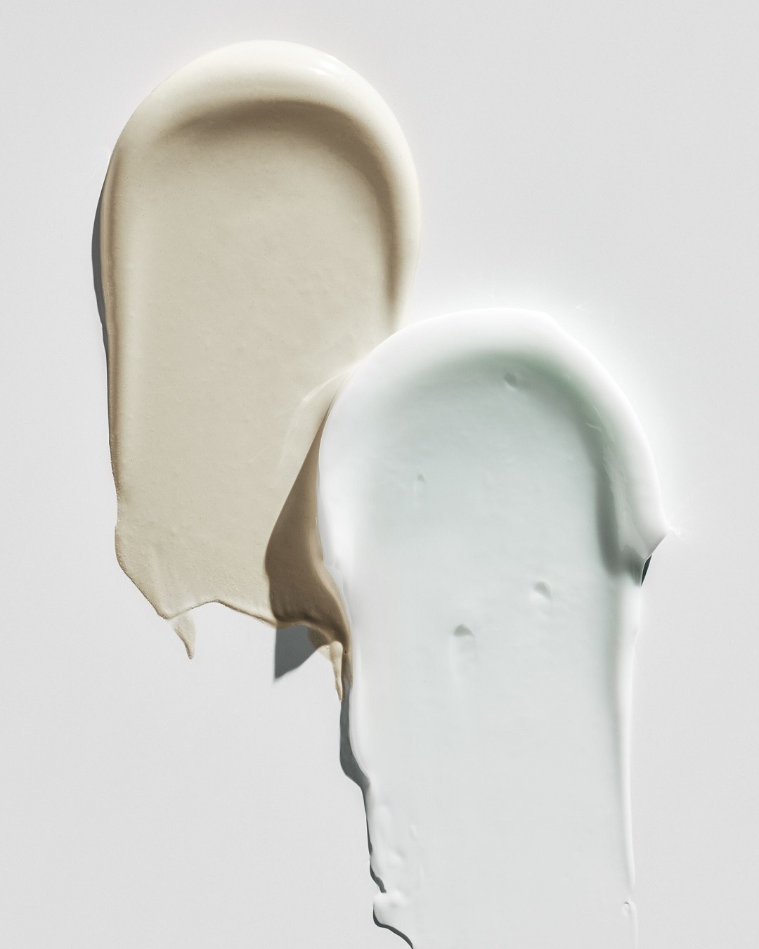 Nahaufnahme von zwei Cremetupfern in Beige und Weiß, die eine reichhaltige Textur und Feuchtigkeitspflege für die Haut suggerieren.