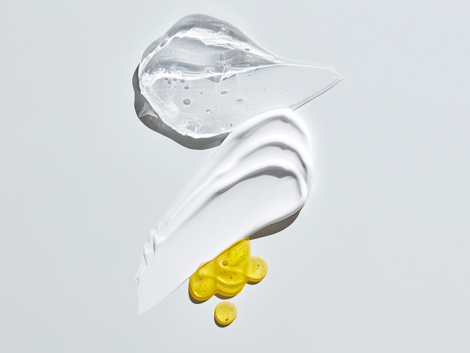 Drei Texturen sind zu sehen: eine klare Geltextur, eine weiße Creme und ein gelbes Öl, die die Vielfalt der Inhaltsstoffe in Schönheitsprodukten demonstrieren.