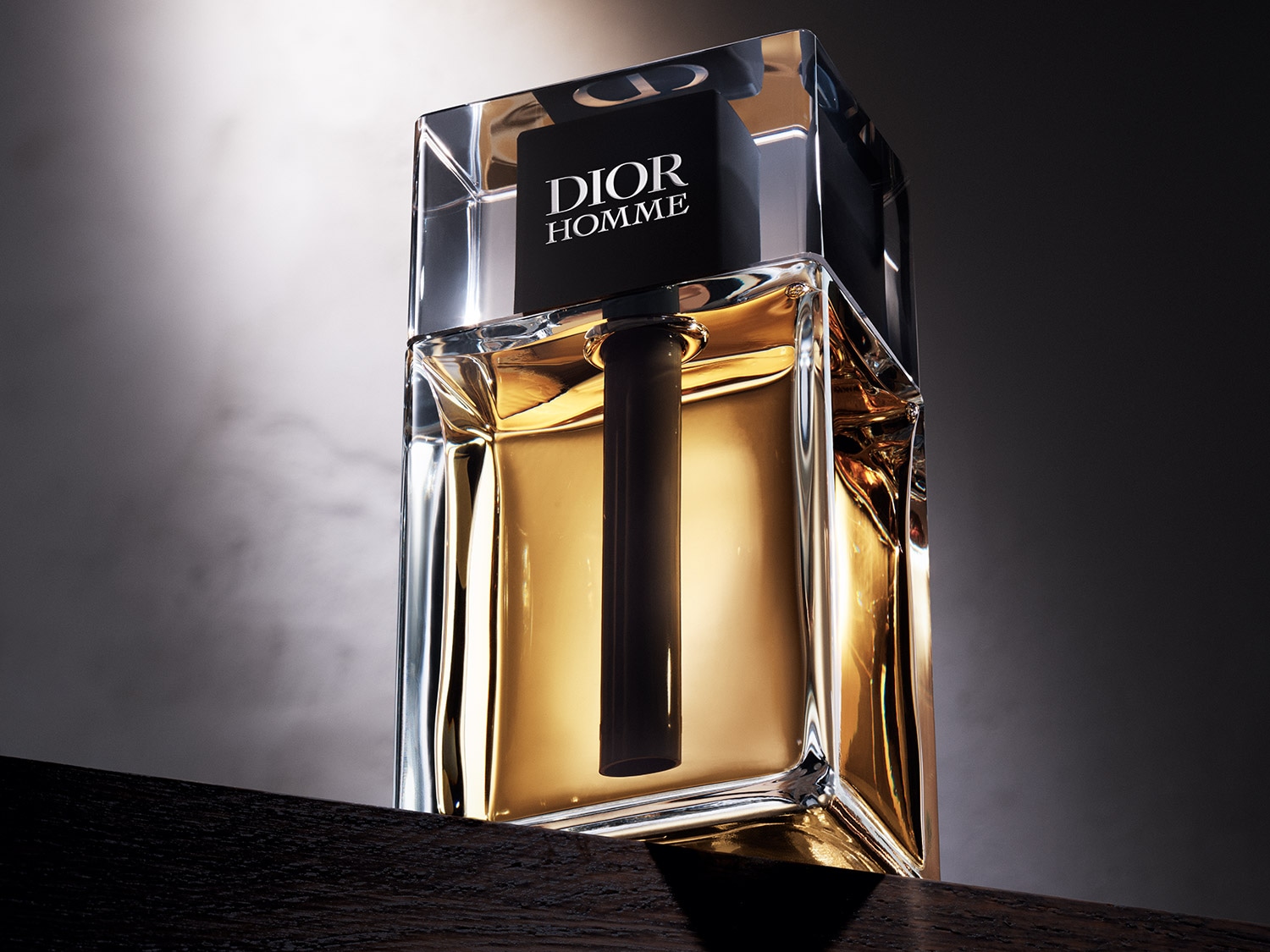 Nahaufnahme des Dior Homme Parfums in einem durchsichtigen Glasflakon mit goldenem Duft, gekrönt von einem schwarzen Verschluss mit dem Dior-Logo.