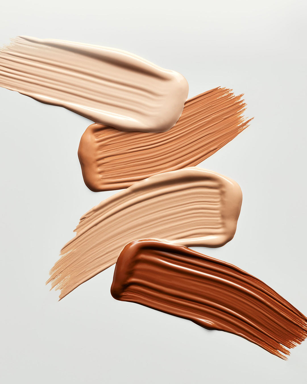 Nahaufnahme von Grundierungsfarbfeldern in verschiedenen Hauttönen, von hellbeige bis dunkelbraun, die die Textur und den Farbton jedes einzelnen Produkts hervorheben.