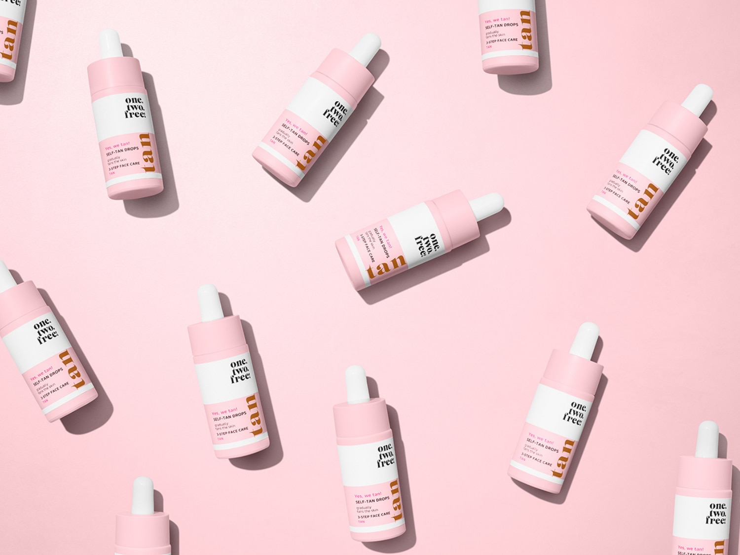 Rožiniame fone išdėlioti „one. two. free!“ savaiminio įdegio lašelių buteliukai su užrašu „Yes, we tan! SELF-TAN DROPS“.