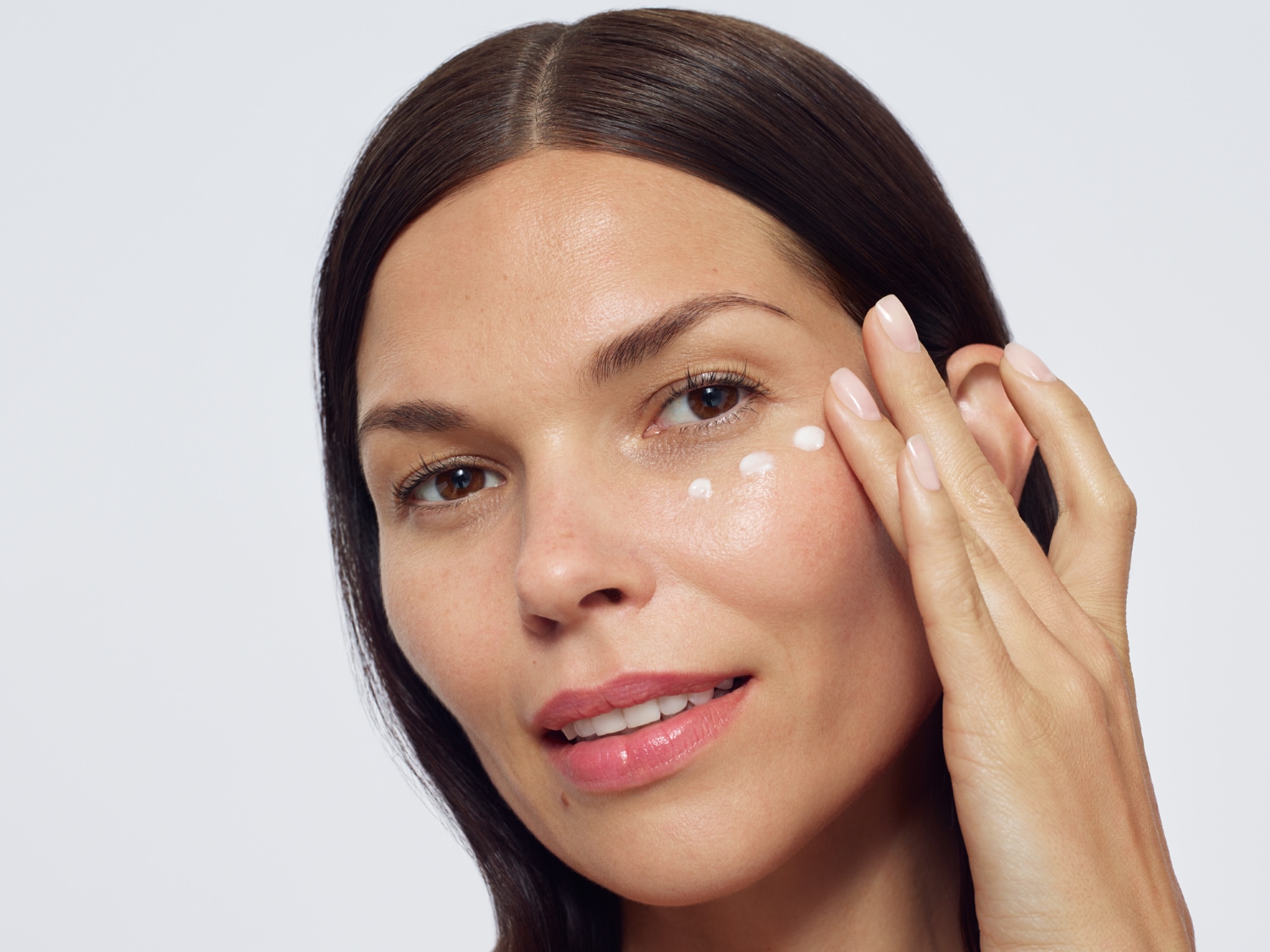 Nahaufnahme einer Frau, die eine weiße Creme um ihr Auge aufträgt, um ihre Haut zu pflegen und ihr Aussehen zu verbessern.