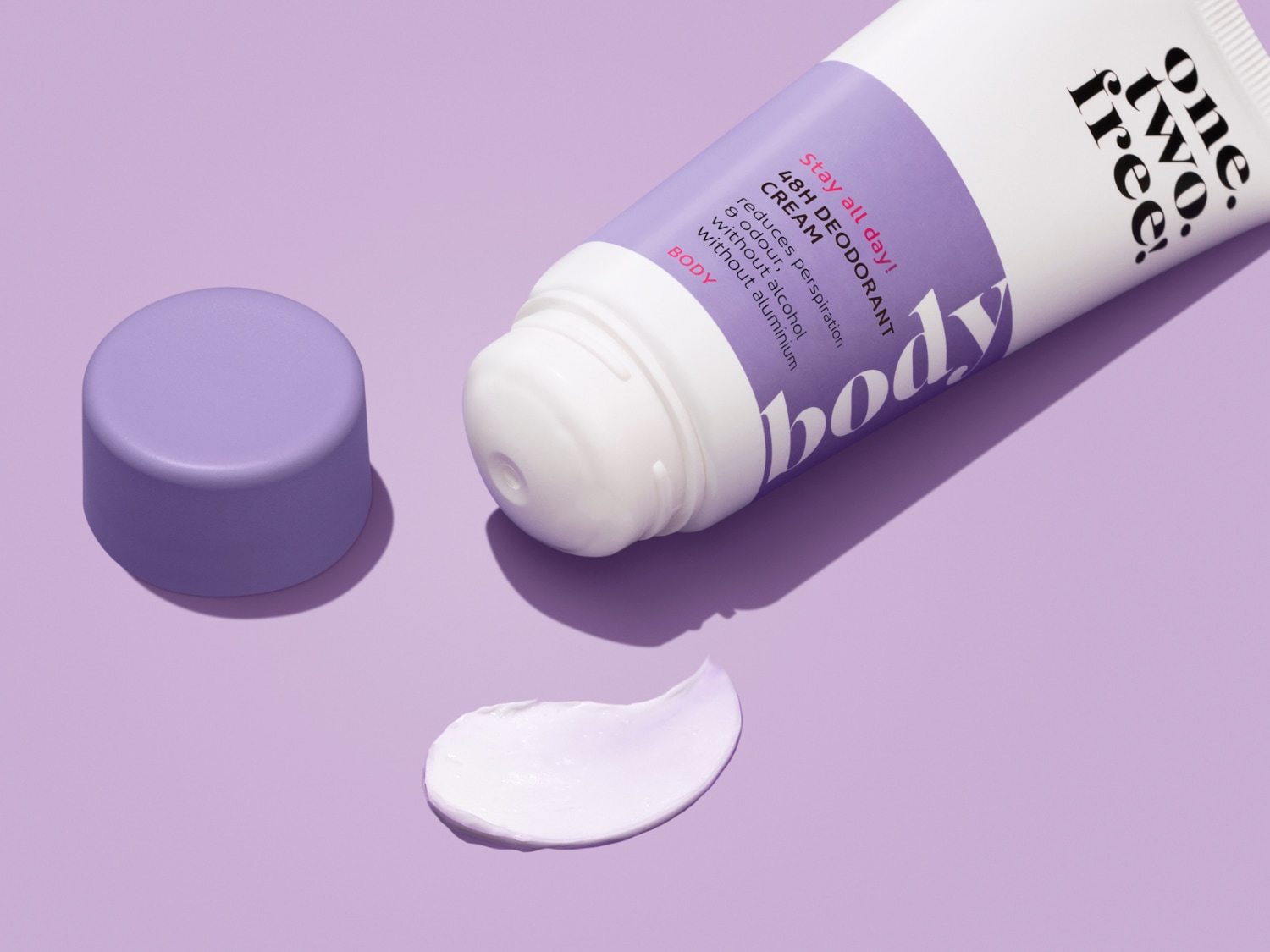 Baltas „One Two Free“ kūno dezodoranto kremas su purpuriniu dangteliu ir užrašu „Stay all day! 48H DEODORANT CREAM“ sumažina prakaitavimą ir kvapą be alkoholio ir aliuminio.