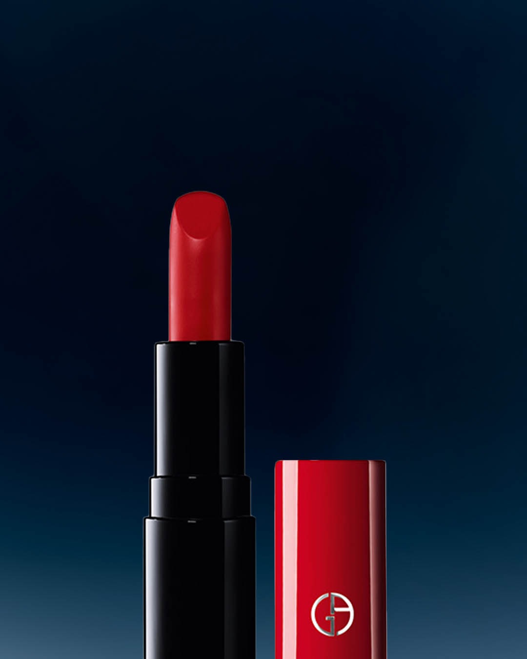 Szminka Giorgio Armani w czarnym opakowaniu z odkręconą czerwoną nakrętką, obok której widoczny jest wkład szminki w intensywnym czerwonym odcieniu.