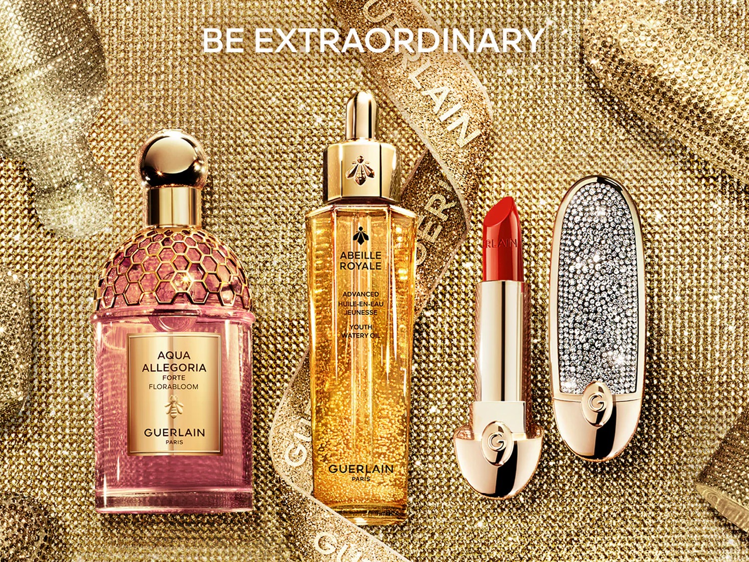 Na złotym tle błyszczą flakon perfum Aqua Allegoria Forte Florabloom, olejek Abeille Royale i szminka Guerlain, a napis "Be Extraordinary" zachęca do wyjątkowości.