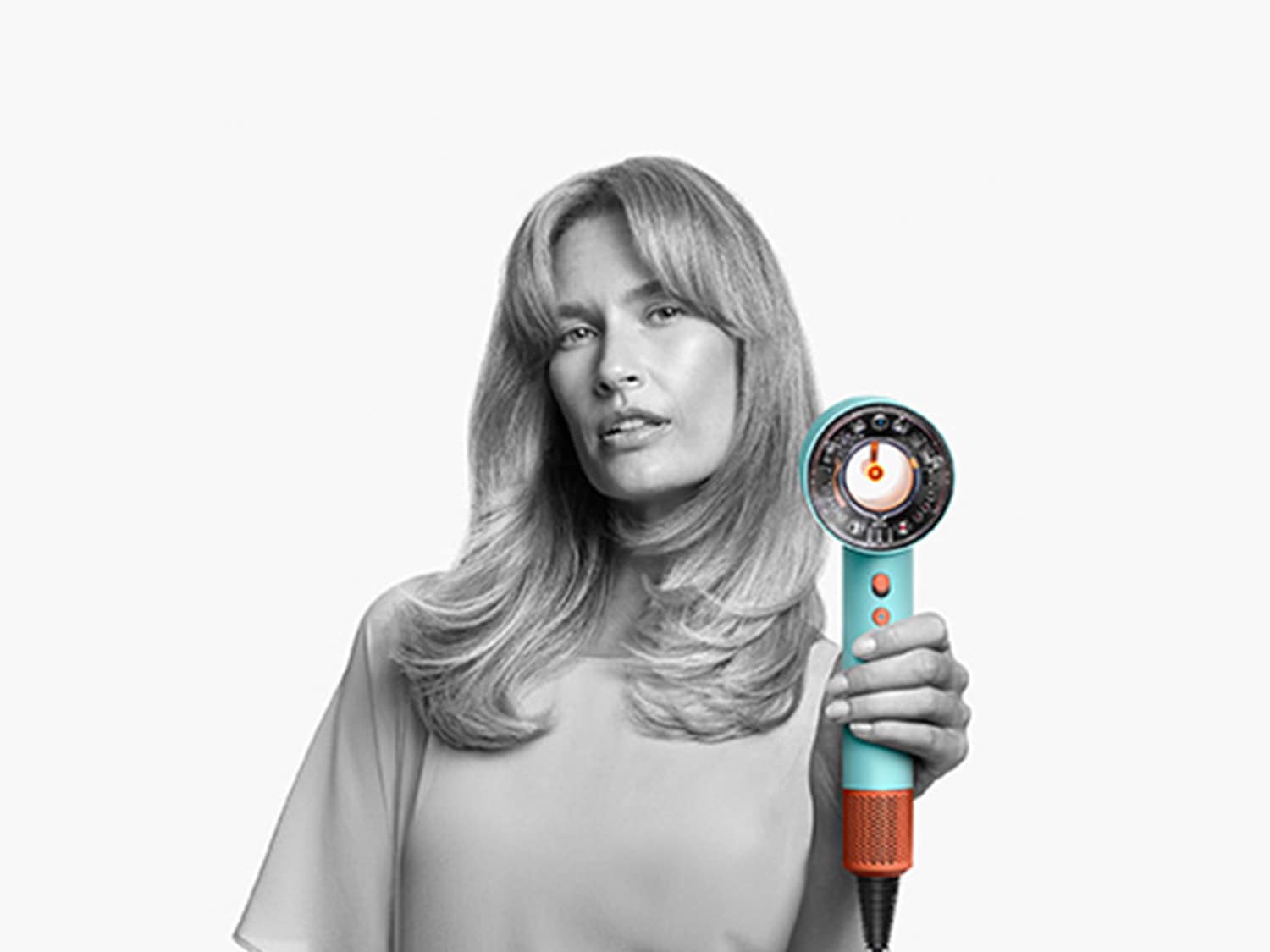 Moteris laiko plaukų džiovintuvą su turkio spalvos korpusu ir oranžiniu pagrindu, demonstruodama jo dizainą ir naudojimą.