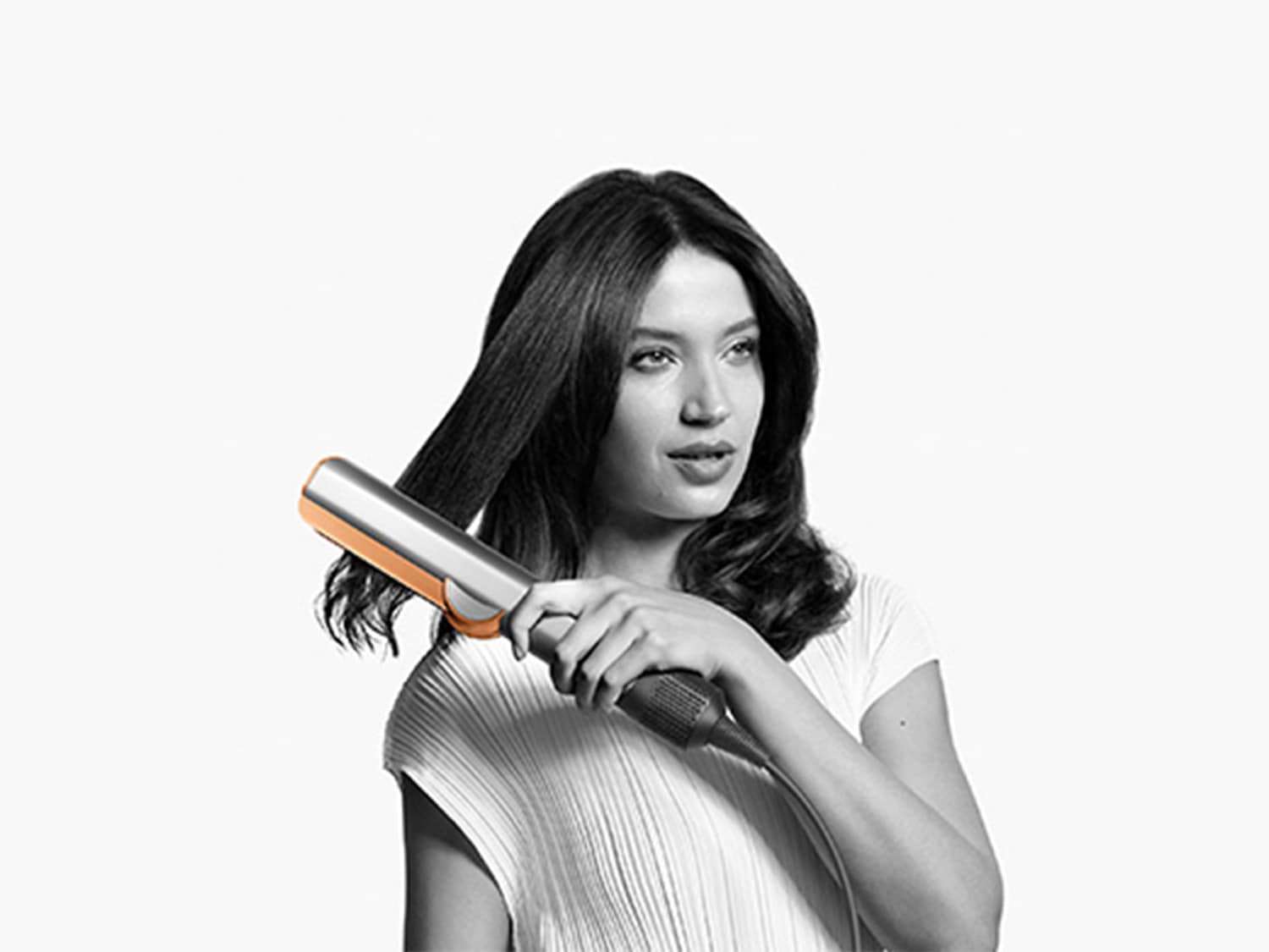 Moteris tiesina plaukus sidabrine ir oranžine plaukų tiesinimo žnyplėmis, kad sukurtų tiesią šukuoseną.