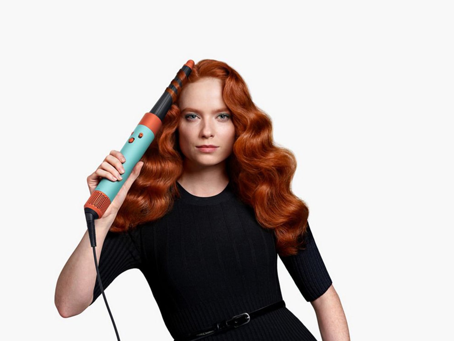 Moteris su ilgais raudonais plaukais pozuoja su turkio spalvos plaukų garbanojimo įrankiu, kad sukurtų tobulas garbanas.
