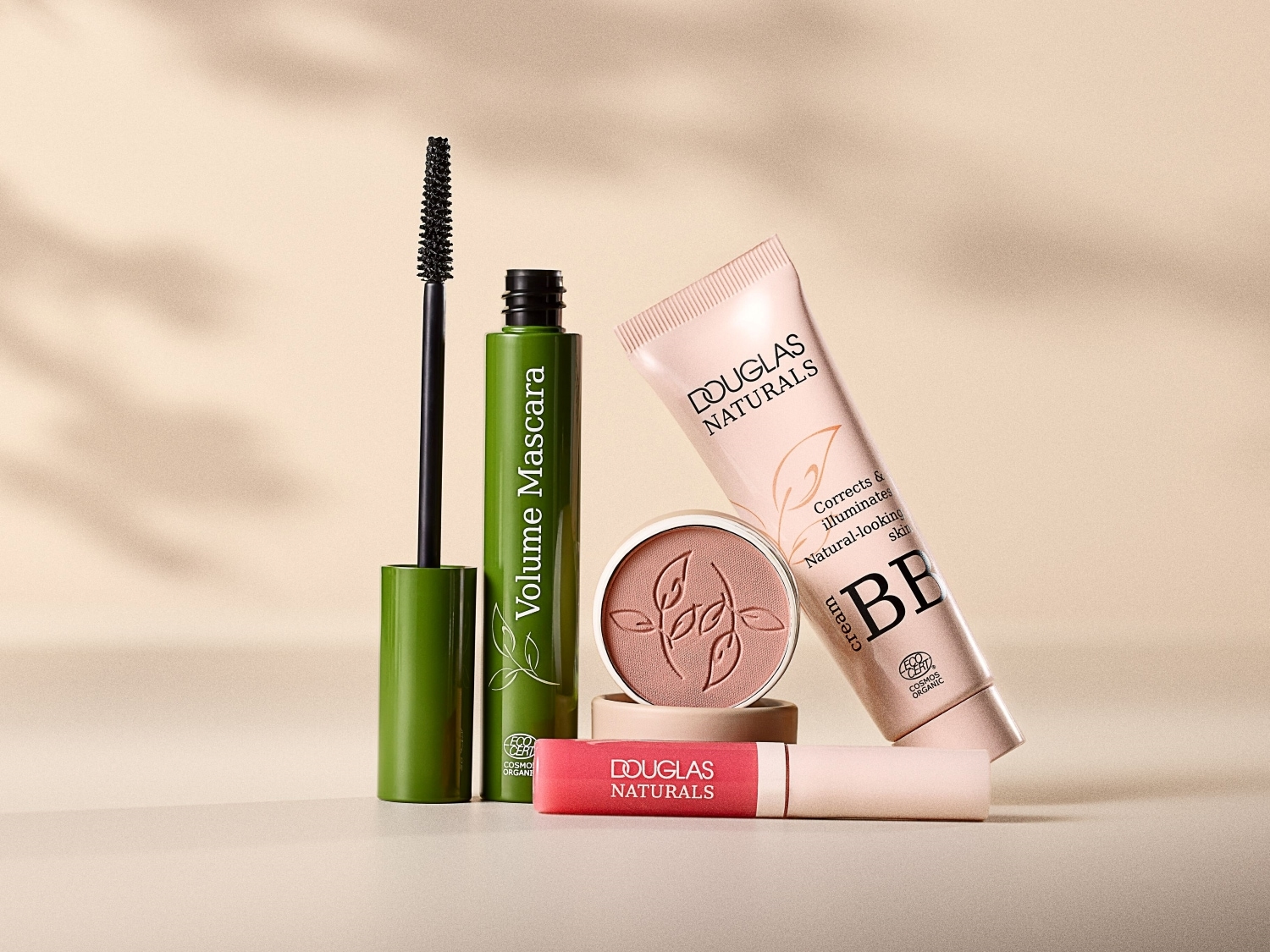 Descubre la colección de maquillaje Douglas Naturals, que incluye máscara de pestañas verde, BB cream en tubo rosa y colorete en polvo compacto.