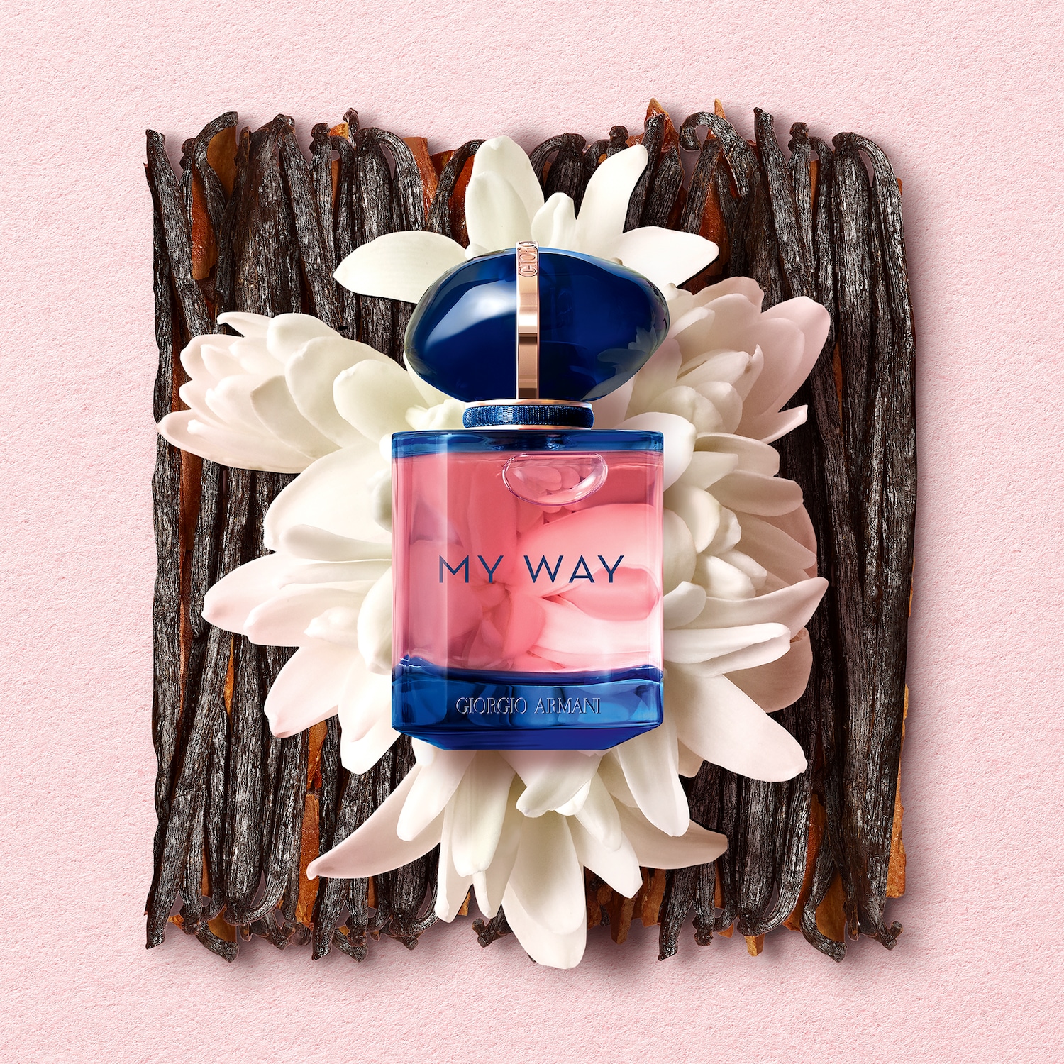 Parfém My Way od Giorgio Armani s růžovou tekutinou v modrém flakonu, obklopený bílými květy a vanilkovými lusky na růžovém pozadí.