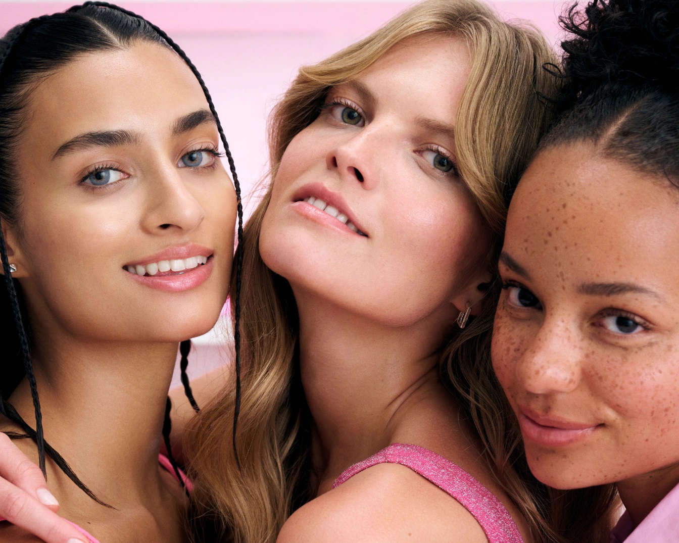Primo piano di tre donne sorridenti con diverse tonalità della pelle e acconciature, che mostrano un incarnato luminoso e sano.