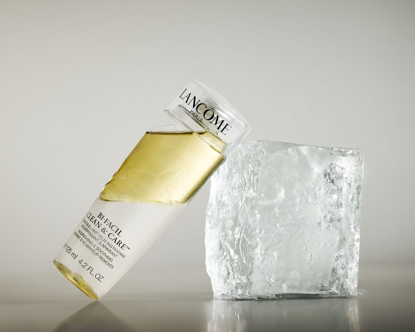 Die Lancôme Bi-Facil Clean & Care Augen-Make-up Entfernerflasche mit durchsichtigem Deckel lehnt an einem Eiswürfel.