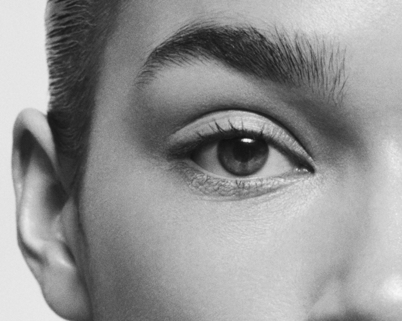 Primo piano in bianco e nero di un occhio marrone con sopracciglio folto, ciglia scure e ombretto chiaro.
