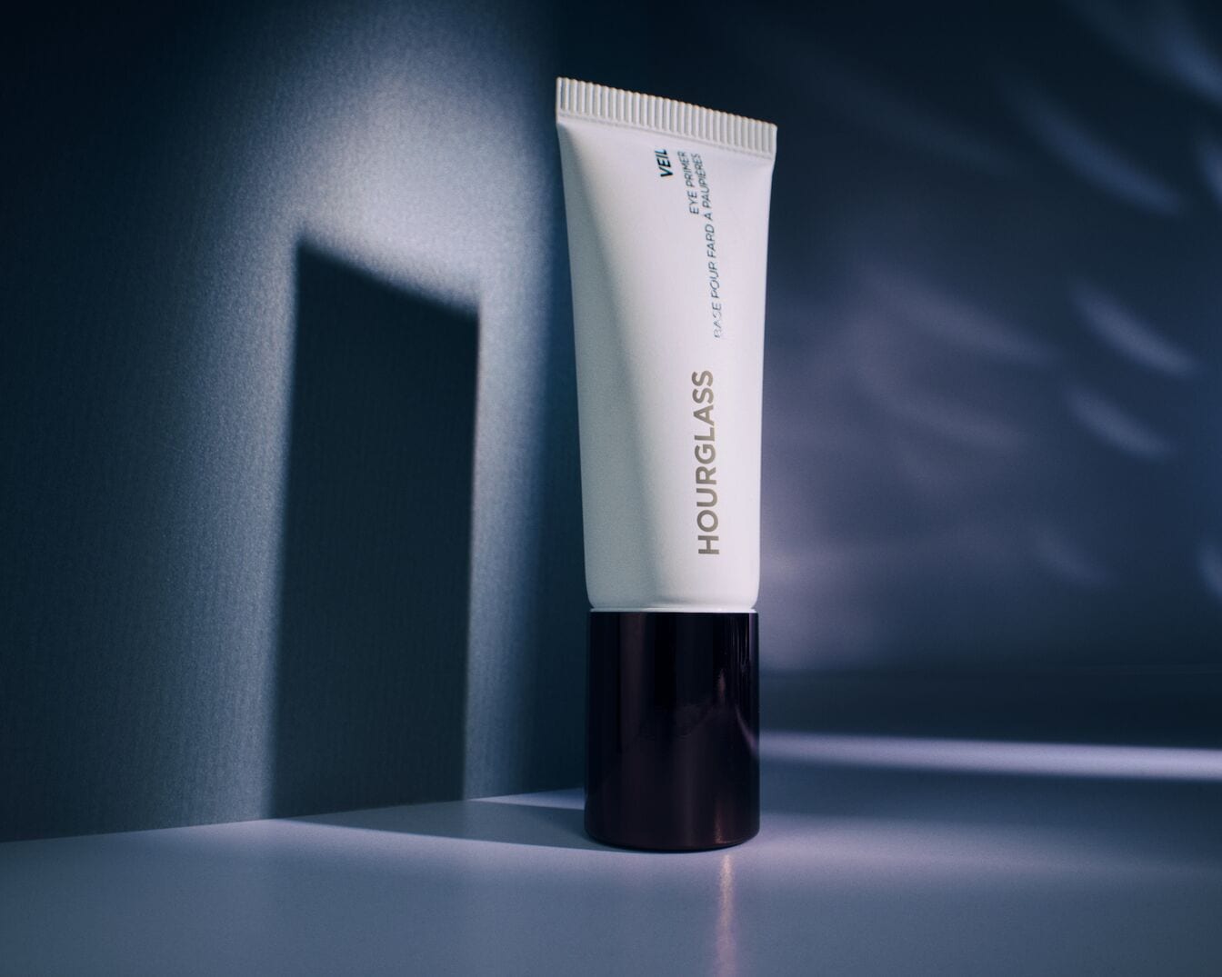 Die Hourglass Veil Eye Primer Tube präsentiert sich in einem eleganten, weißen Design mit einem dunklen Sockel, ideal für eine ebenmäßige Grundlage.