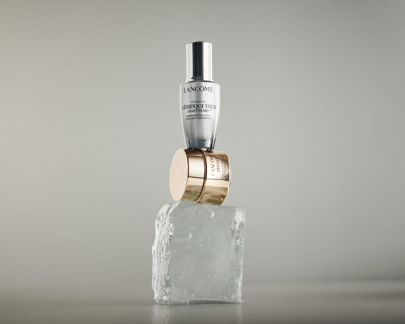 Na kostce lodu ustawione są produkty Lancôme: Advanced Génifique Yeux Light-Pearl w srebrno-białym opakowaniu i Absolue w złotym słoiczku.