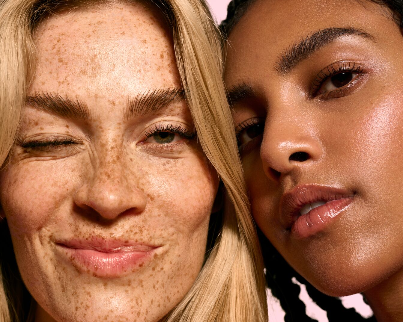 Twee close-ups van gezichten, één met sproeten en blond haar dat knipoogt, en de ander met een gladde huid en donker haar, beide met glanzende lippen.