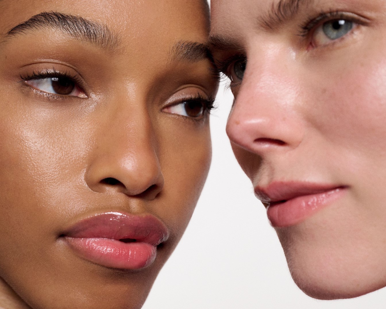 Twee vrouwen met een verschillende huidskleur staan dicht bij elkaar, hun gezichten stralen met een natuurlijke glans en subtiele lipgloss.