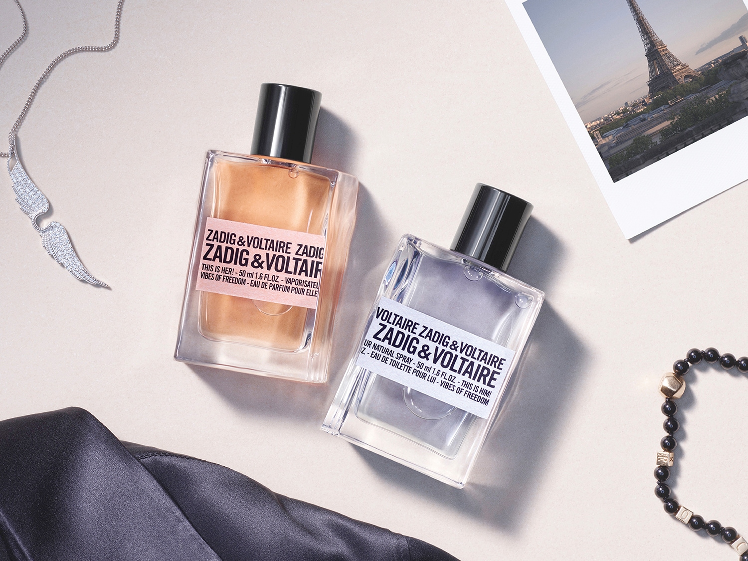 Zadig & Voltaire Parfums: This is Her! Eau de Parfum und This is Him! Eau de Toilette, beide in klaren Glasflakons mit schwarzen Kappen, umgeben von Schmuck und einem Foto des Eiffelturms.