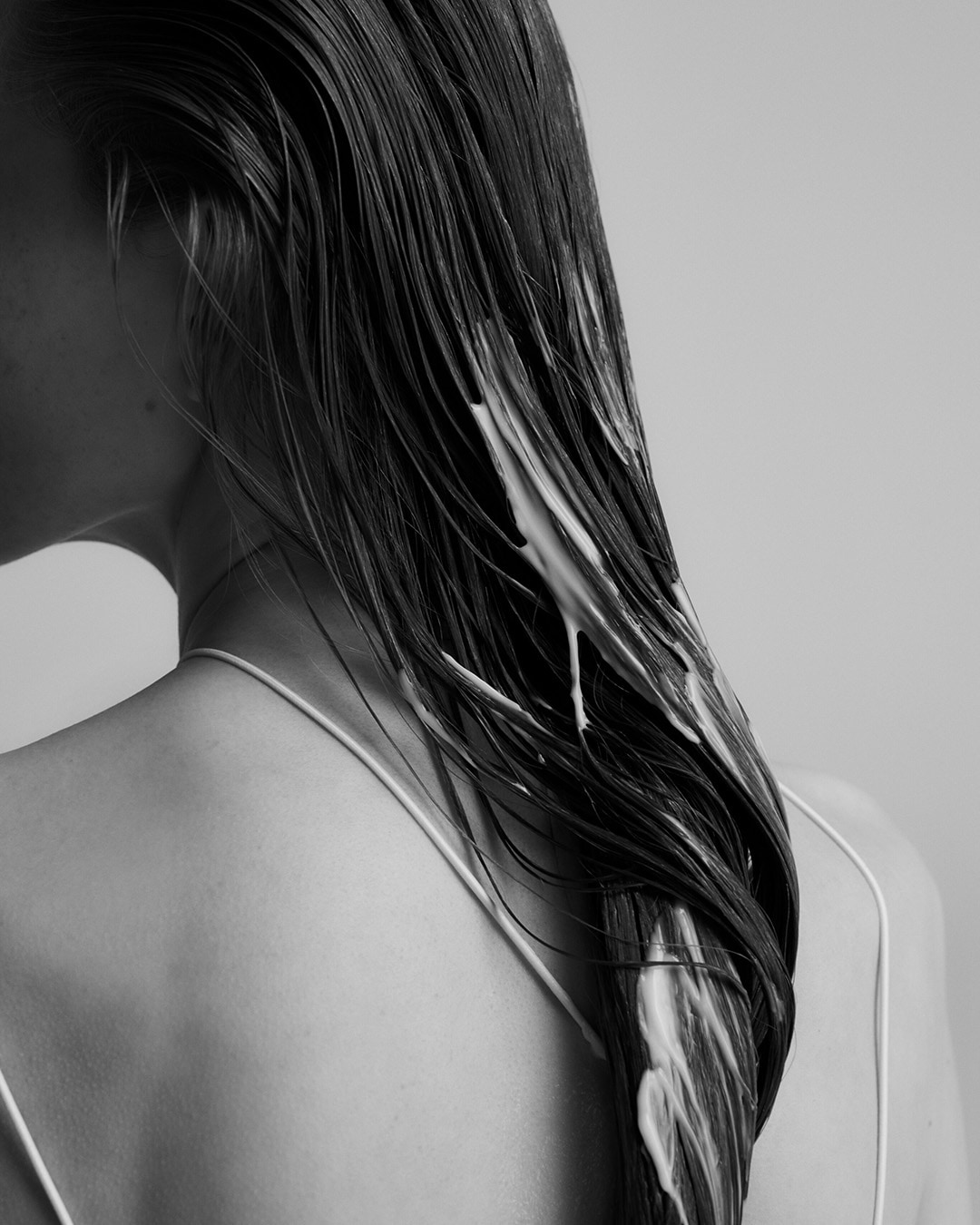 Czarno-białe zdjęcie przedstawia włosy kobiety, na które nałożono kremową odżywkę, podkreślając pielęgnacyjny charakter produktu.