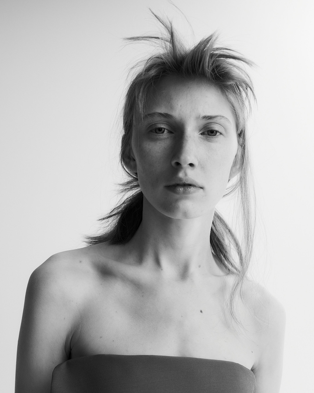 Czarno-białe zdjęcie kobiety z włosami zaczesanymi do góry, ubranej w tubę, z poważnym wyrazem twarzy.