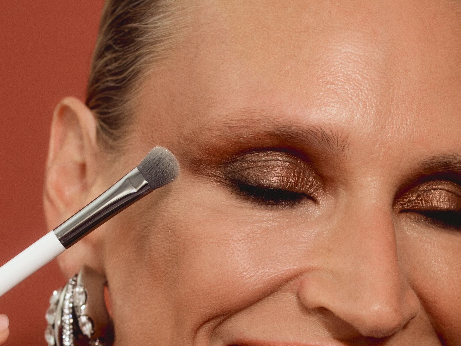 Nahaufnahme einer Frau, die mit einem Pinsel goldfarbenen Lidschatten auf ihr Augenlid aufträgt, um einen strahlenden Look zu erzielen.