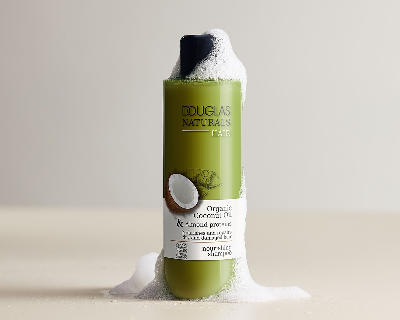 Grüne Flasche Douglas Naturals Haarshampoo mit Kokosöl und Mandelproteinen, umgeben von Schaum, für die Pflege von trockenem und strapaziertem Haar.