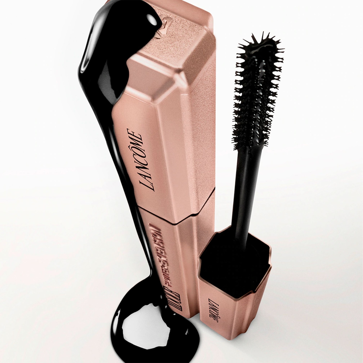 Die Lancôme Mascara präsentiert sich in einer eleganten, roséfarbenen Verpackung, umhüllt von einem Klecks tiefschwarzer Farbe, die die intensive Formel hervorhebt.