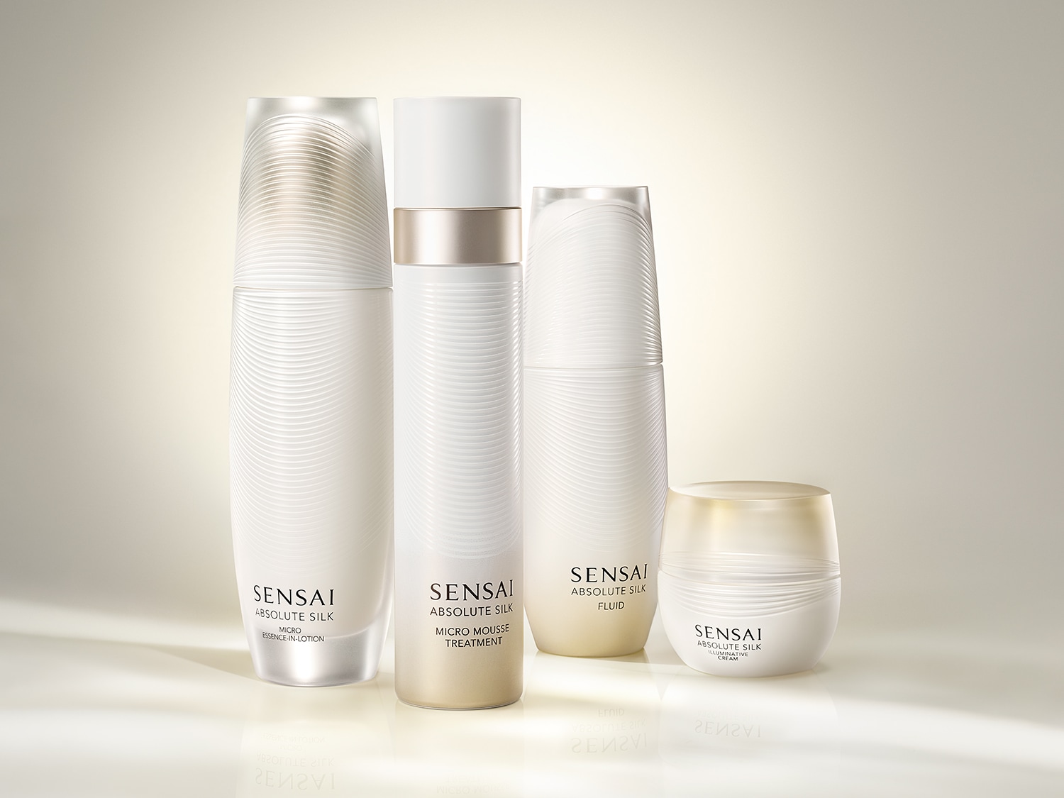 Vier SENSAI Absolute Silk producten in witte verpakkingen met zilveren details, waaronder een essence-in-lotion, micro mousse treatment, fluid en illuminative crème.