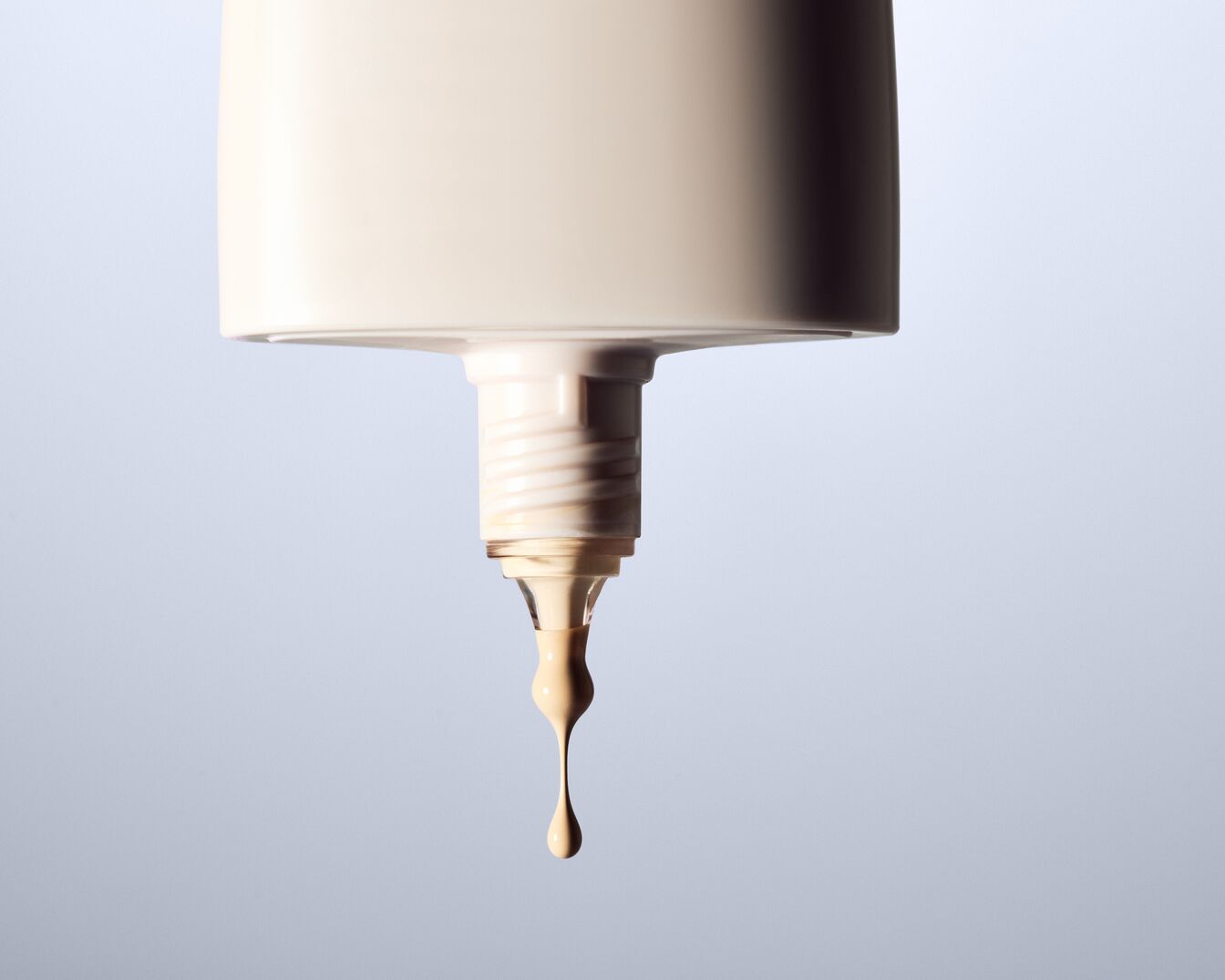 Nahaufnahme einer beigen Foundation-Flasche, aus der ein Tropfen Make-up austritt, ideal für einen ebenmäßigen Teint.