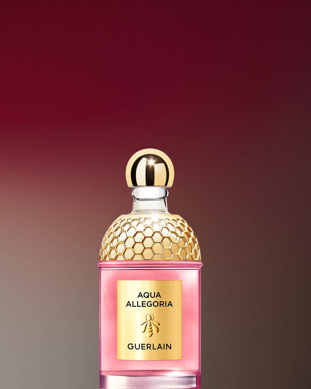 Różowy flakon perfum Aqua Allegoria marki Guerlain z złotą nakrętką i etykietą, prezentowany na rozmytym tle w odcieniach różu i brązu.