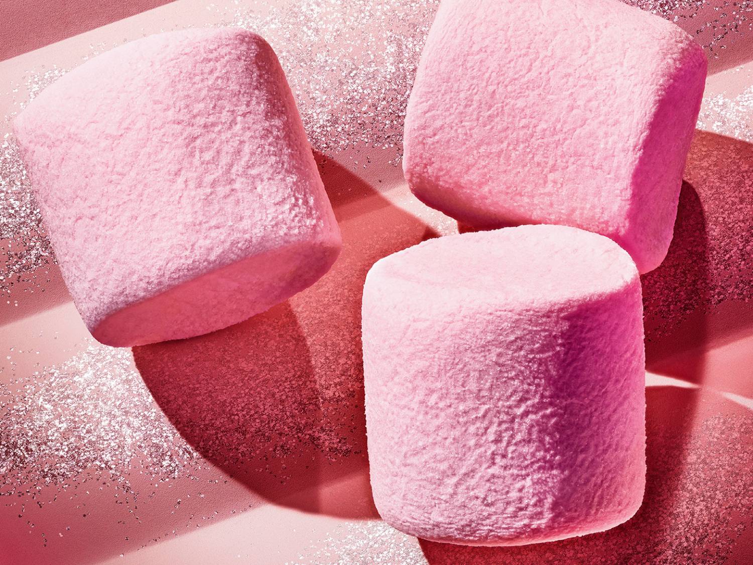 Három rózsaszín pillecukor látható rózsaszín csillogó háttéren, édes és ünnepi hangulatot árasztva.