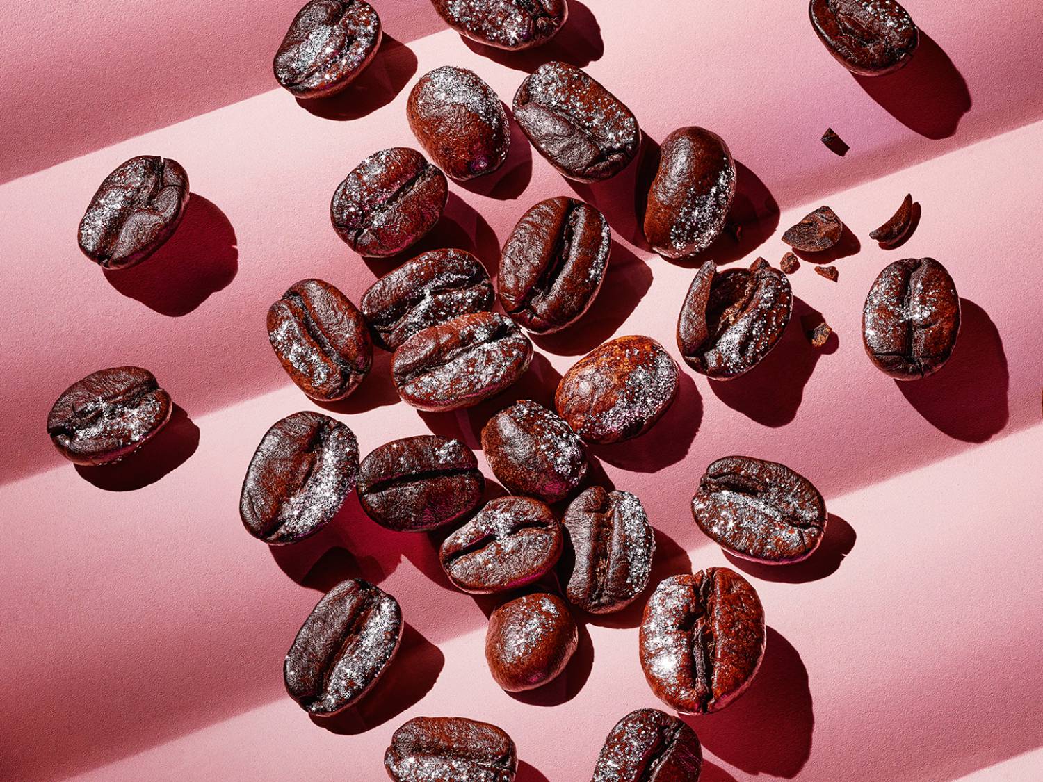 Kávészemek láthatók rózsaszín alapon, finom, ezüstös porral meghintve, melyek a kávézás élvezetére csábítanak.