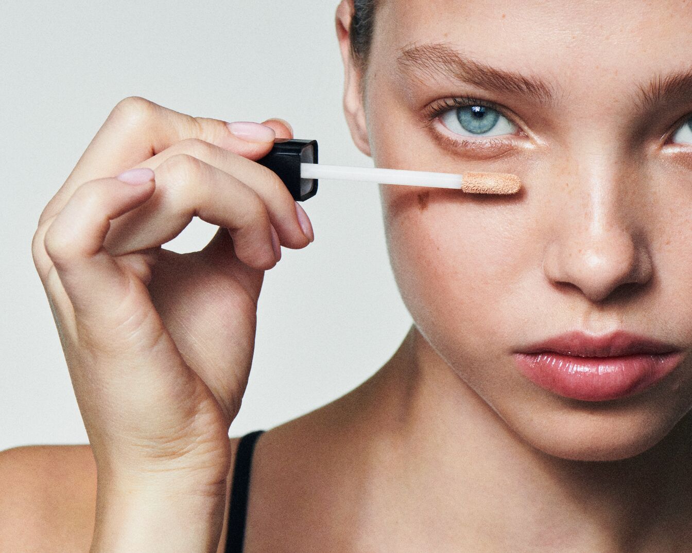 Nahaufnahme einer Frau, die mit einem Applikator Concealer unter ihrem Auge aufträgt, um Hautunreinheiten abzudecken.