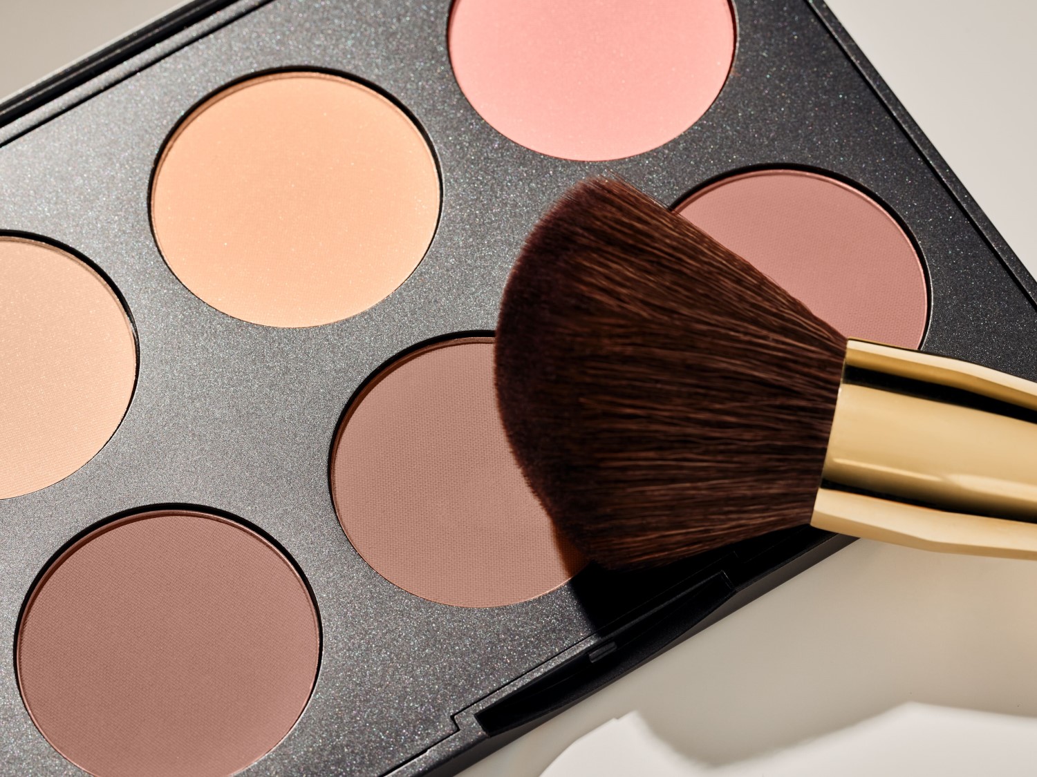 Nahaufnahme einer Make-up-Palette mit verschiedenen Farbtönen und einem Pinsel, ideal zum Konturieren und für einen strahlenden Teint.