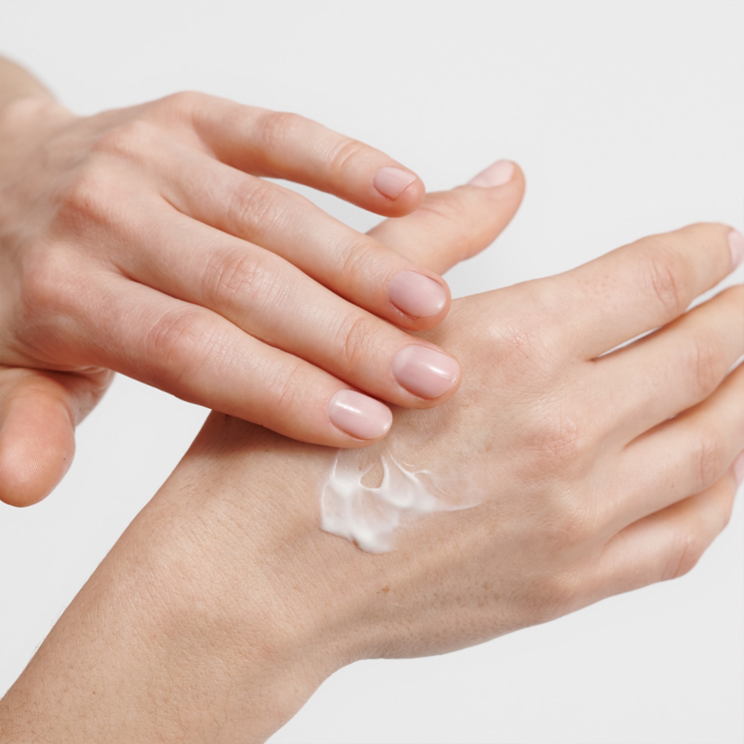 Nahaufnahme von zwei Händen, wobei eine Hand eine kleine Menge weißer Creme auf den Handrücken der anderen Hand aufträgt.