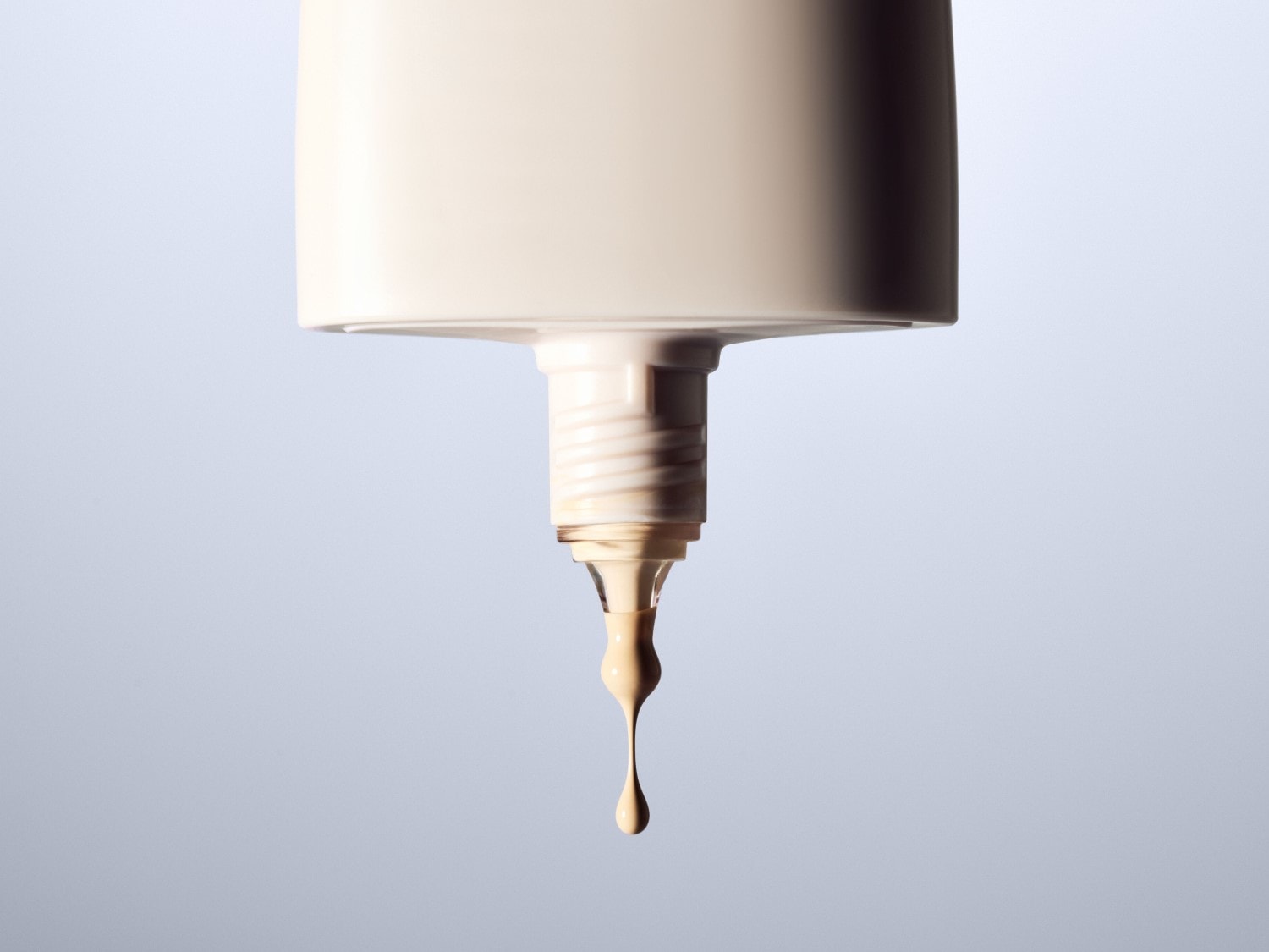 Nahaufnahme einer beigen Foundation-Flasche, aus der ein Tropfen Make-up austritt, der die cremige Textur und den Farbton des Produkts hervorhebt.